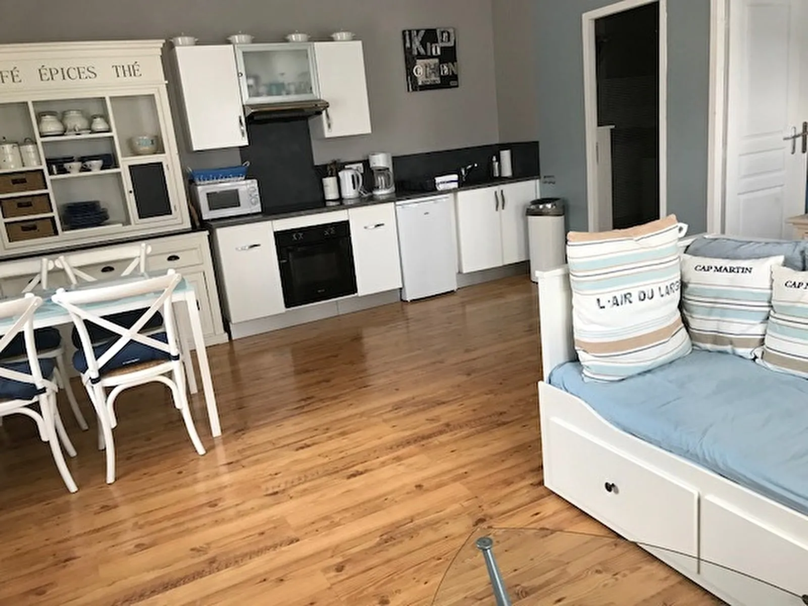 La pièce de vie du Grand Mistral : kitchenette blanche, banquette-lit, table et chaises sur un parquet clair