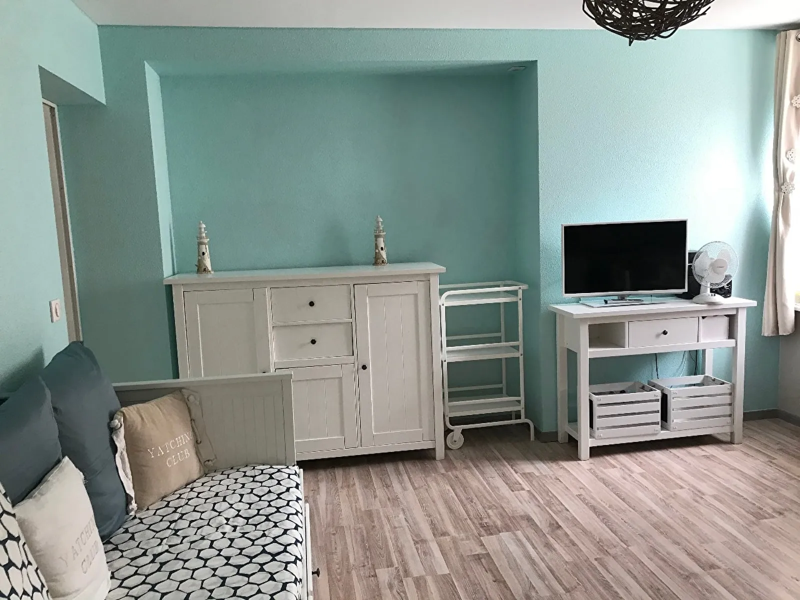 La pièce de vie du Petit Mistral : canapé, commode et télévision, murs vert d’eau